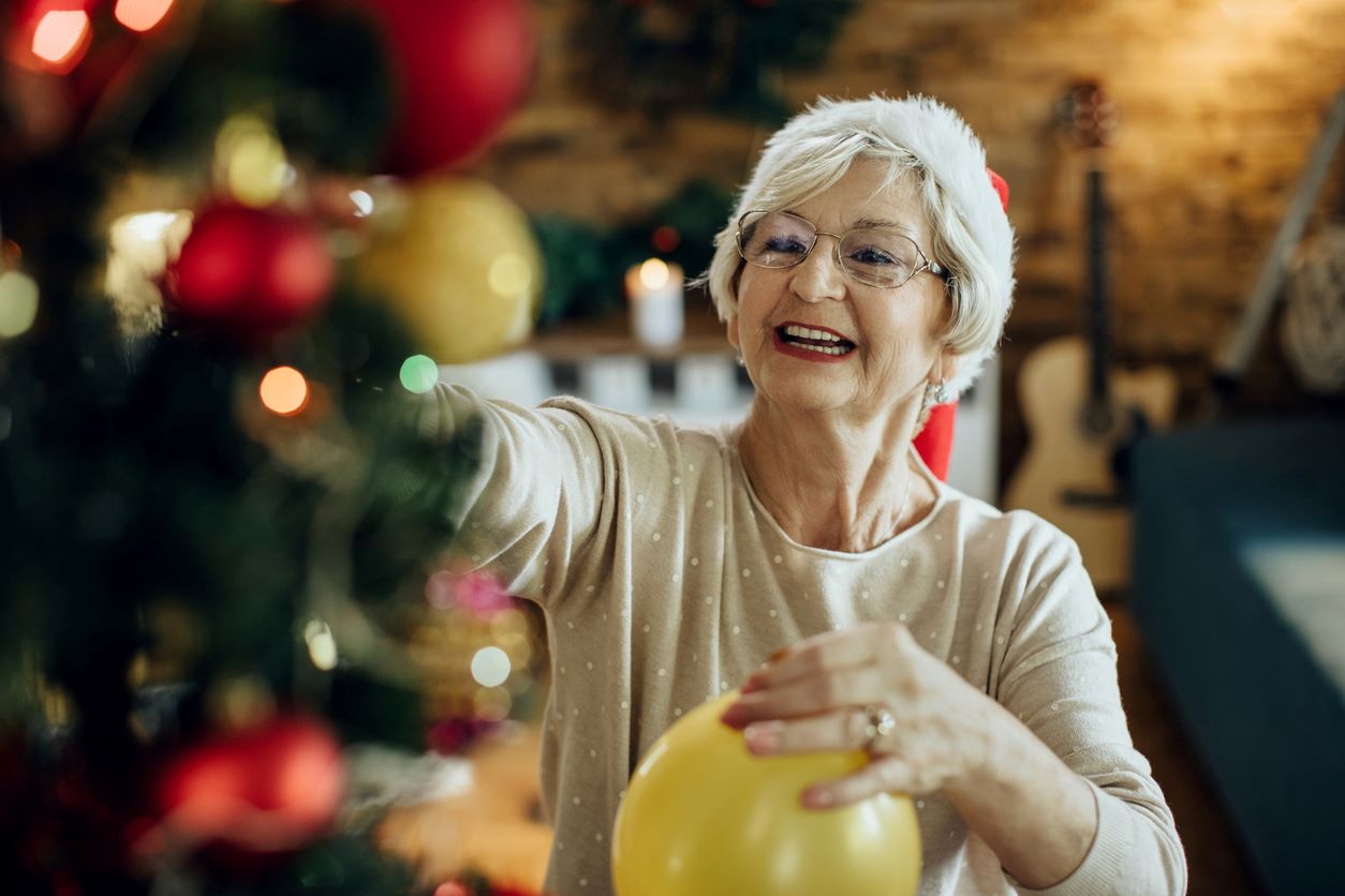 A grandmother and granddaughter put ornaments on a Christmas tree.