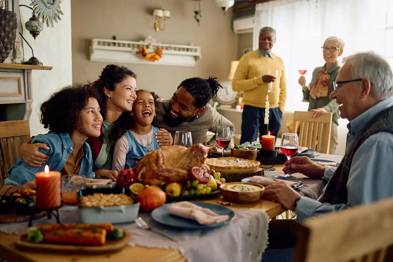 A smiling family hugging at the dinner table and looking at a spread of healthy holiday foods.