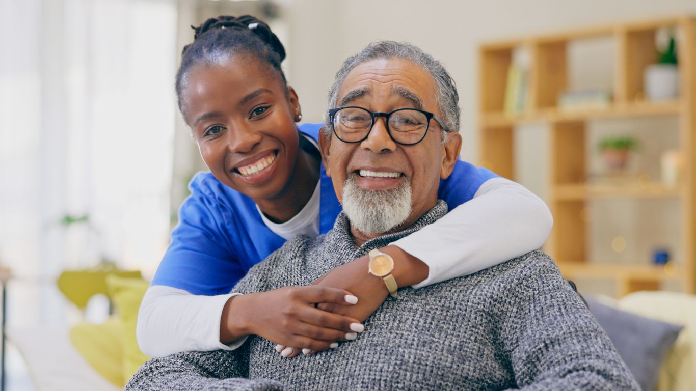 A caregiver and per patient smiling as she wraps her arms around him.