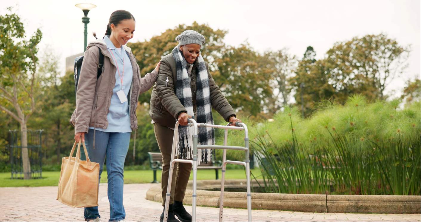 A nurse and her senior patient walk through a nature park.