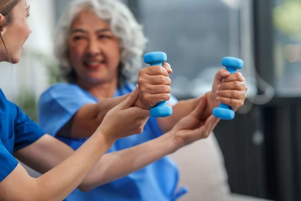 A caregiver helps a senior patient exercise with dumbbells.
