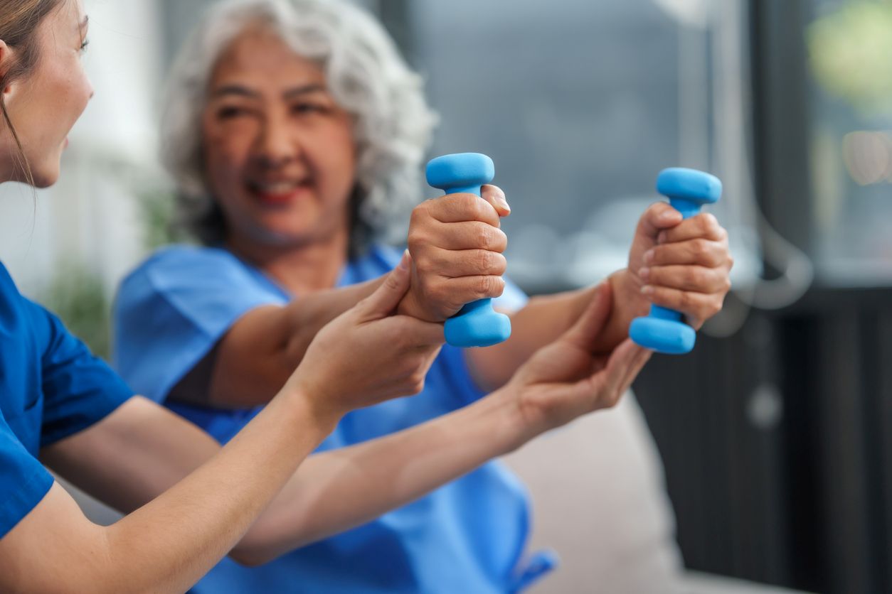 A caregiver helps a senior patient exercise with dumbbells.