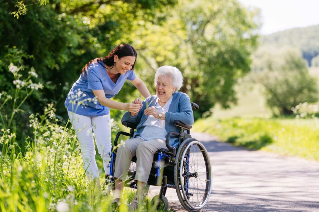 A caregiver and her senior patient in a wheelchair enjoy picking flowers.