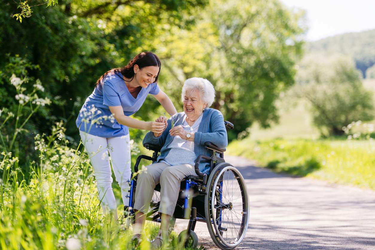 A caregiver and her senior patient in a wheelchair enjoy picking flowers.