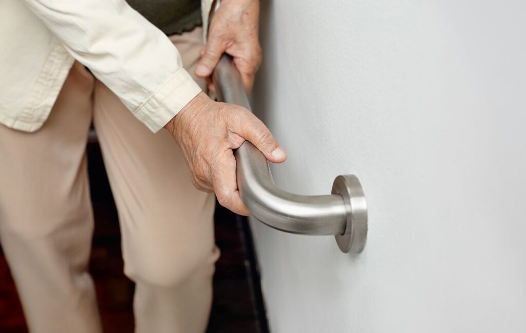 A senior climbs up the stairs with a safety rail.