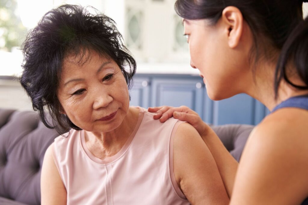 An adult daughter sits on the couch with her mother, talking.