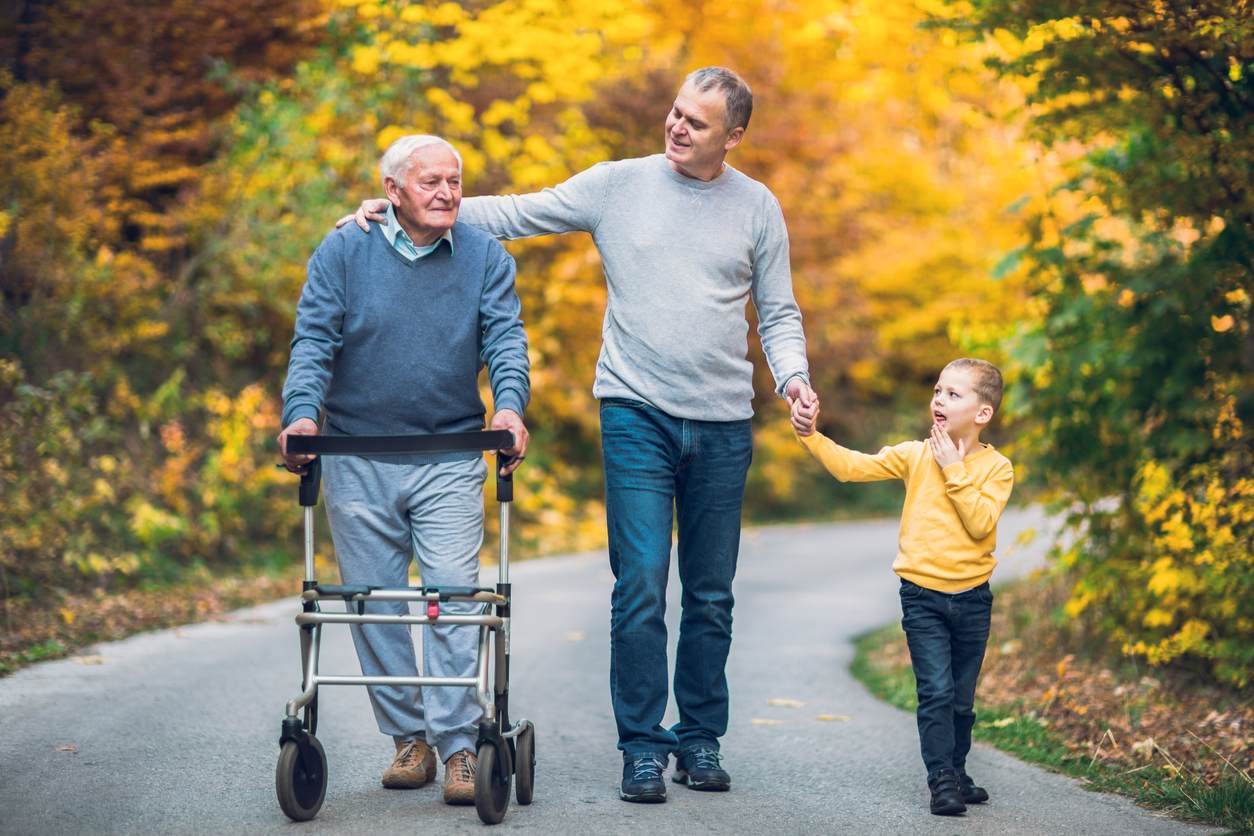 A man, his child, and his father walk along a paved path.
