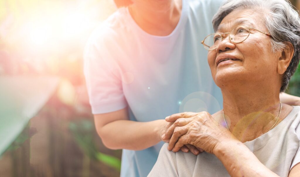 A caregiver holds the hand of her patient sitting in the sunshine