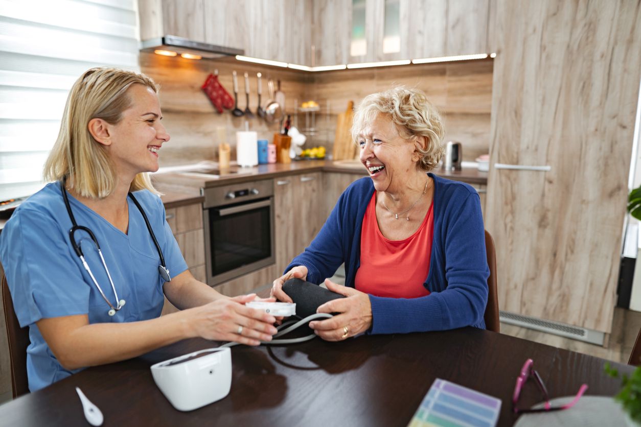 A caretaker smiles and laughs with her client as they measure her vitals.