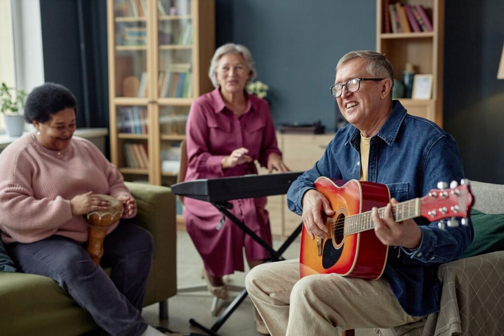 A group of seniors happily make music together on a darbuka, keyboard, and acoustic guitar.