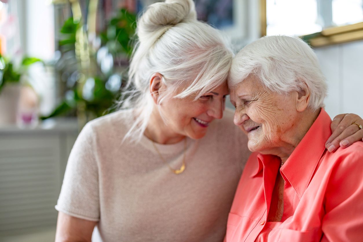 Adult daughter hugging her aging mother while sitting together in a bright home.